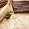 Display of packaging materials including Hero Pack compostable mailer bags, a ball of green yarn, Care labels and a wrapped t-shirt in the tissue paper with a green design.