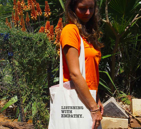 Female using a Long Handle Calico Bag. Graphic is stacked words in black The text reads Listening with Empathy.