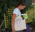Female using a Short Handle Shopper Style Calico Bag, natural colour.  Design in blue and pink.  Surfboard with banner saying Wind Festival.  Text reads Carnarvon Western Australia.  West Coast. Surf Side. Indian Ocean. 6701. Chasing the wind.