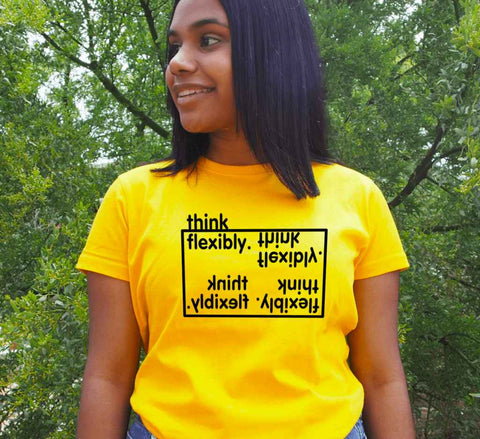 Female wearing a yellow fitted short sleeve t shirt with a design in black.  Graphic is the words Think Flexibly written within a box in 4 different directions.  The word Think is located outside the box.