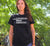 Female in a garden wearing a black Fitted Short Sleeve T Shirt. Graphic is stacked words in white. The text reads Listening with Empathy.