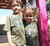 Boy and Girl outside a house wearing Khaki Short Sleeve T Shirt.  Design in blue and pink.  Surfboard with banner saying Wind Festival.  Text reads Carnarvon Western Australia.  West Coast. Surf Side. Indian Ocean. 6701. Chasing the wind.