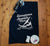 Black tea towel flat lay in a kitchen.   Design in white.  Graphic is a silhouette of a kite surfer with the text Carnarvon Western Australia.  It's all About the Summer Wind.