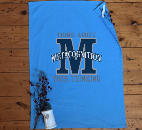 Flat lay Light Blue Tea Towel in a kitchen. Graphic large letter M. The text reads Metacognition, think about your thinking.