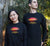 Male and Female in a garden wearing black long sleeve t shirts.  Text in yellow Carnarvon, Westerm Australia.  Graphic of palm trees and birds in silhouette against a sunset.