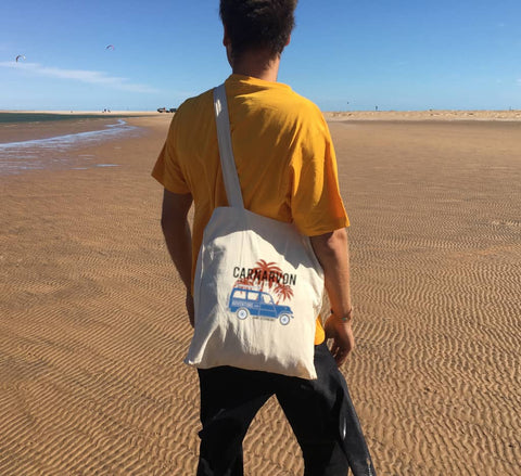 Male on a beach using a Long Handle Calico Bag.  Graphic of a Troop Carrier with Palm Trees.  Text reads Carnarvon, Western Australia Camp Responsibly.