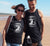 Male and Female at the beach wearing black singlet tank t shirts.  Design is in white.  The graphics are of a silhouette of a kite surfer with the text Wind Riders, Carnarvon Western Australia,