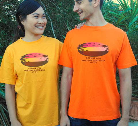 Male and female in a garden wearing short sleeve t shirts.  She is wearing Golden Yellow he is wearing orange.  Text in red Carnarvon, Westerm Australia.  Graphic of palm trees and birds in silhouette against a sunset.