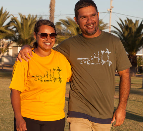 Female wearing yellow and male wearing khaki short sleeve T Shirts. The design is in black on yeloow - or white on haki. The graphic is an outline image of a seed growing in stages. The text is nurture by nature.