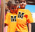 Boy and girl ouside a house with arms around eachother wearing orange kids Short Sleeve T Shirt. Graphic large letter M. The text reads Metacognition, think about your thinking.
