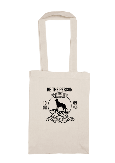Long handle calico bag with the design. The graphic is one colour.  There is a circle outline with a silhouette of a dog standing on a rocky outcrop.  Around the circle the text says - Be the person your dog thinks you are, Nurture by Nature.  On either side of the circle there is text that is split - it says 19-69, Best Mate, Wild Life