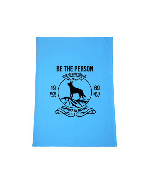 Bright Light Blue Tea Towel with design. The graphic is one colour.  There is a circle outline with a silhouette of a dog standing on a rocky outcrop.  Around the circle the text says - Be the person your dog thinks you are, Nurture by Nature.  On either side of the circle there is text that is split - it says 19-69, Best Mate, Wild Life