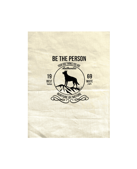 Natural Tea Towel with design. The graphic is one colour.  There is a circle outline with a silhouette of a dog standing on a rocky outcrop.  Around the circle the text says - Be the person your dog thinks you are, Nurture by Nature.  On either side of the circle there is text that is split - it says 19-69, Best Mate, Wild Life
