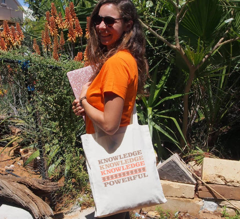 Female in a garden using a Long Handle Calico Bag, natural colour.  Graphic is stacked words in shades of brown and orange.  The text reads Knowledge, repeated 3 times, and Powerful.