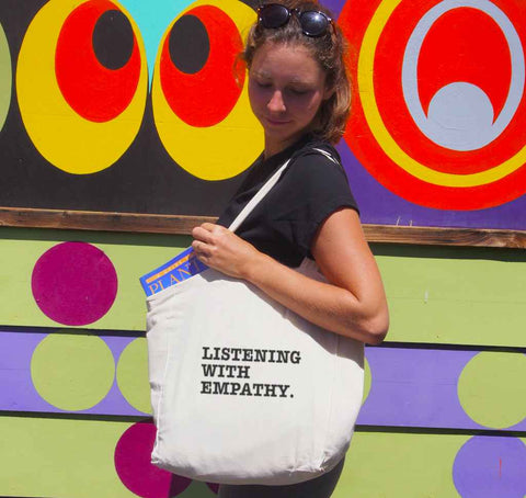 Female using a short Handle Calico Shopping Bag. Graphic is stacked words in black The text reads Listening with Empathy.