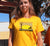 Female wearing Golden Yellow fitted T Shirt.  Graphic of a yellow sunset with birds, a tree and a dog in silhouette. Text reads Sunshine of My Life, Best Mate