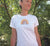 Female in a garden wearing a White fitted Short Sleeve T Shirt.  Graphic is a rainbow with a leaf with the statement, cool, calm and collected.