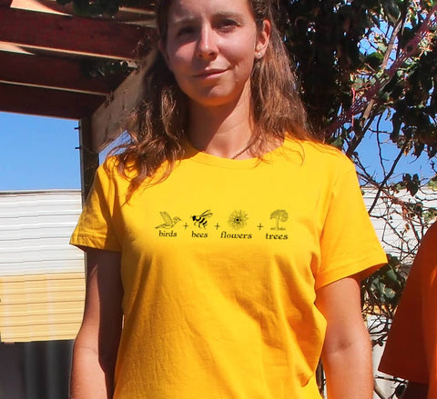Female wearing a Yellow fitted Short Sleeve T Shirt. The design is in black. The graphics are 4 outline images with words underneath and a plus sign in between. The images are of a bird, bee, flower and tree.